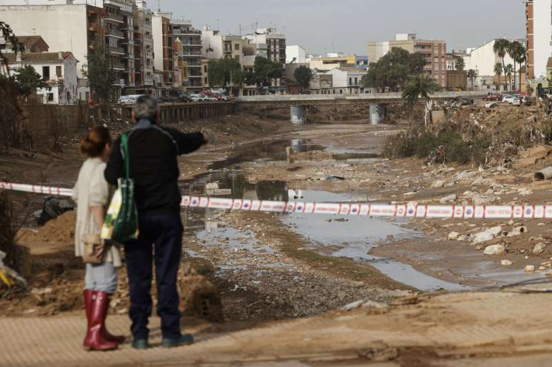 Dos personas observan el barranco del Poyo a su paso por Paiporta, este lunes. EFE/Biel Aliño
