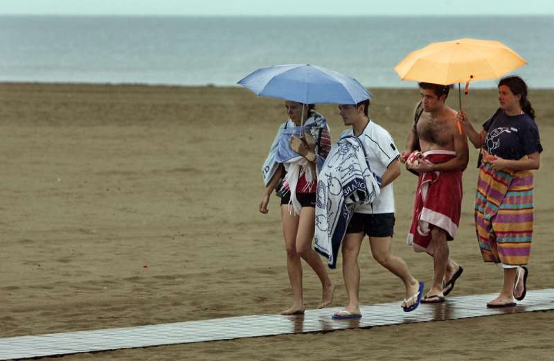 Imagen de archivo de varios jóvenes resguardándose de la lluvia en la playa de la Malvarrosa de Valencia. / EFE
